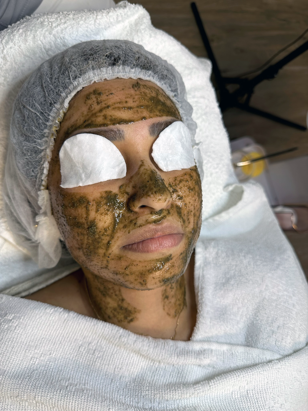 Eine Kundin erhält eine Gesichtsbehandlung mit einer nährenden Gesichtsmaske und bedeckten Augen, während sie entspannt auf einer Behandlungsliege in einem Kosmetikstudio liegt.